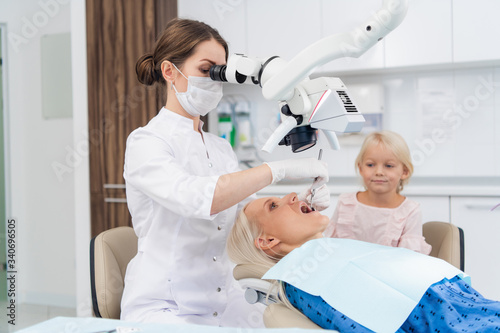 A dentist examines the oral cavity of her patient on the dentist s chair with the help of a special medical appliance