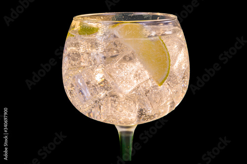 Alcohol drink (gin tonic cocktail) with lemon and ice on black background. Iced cocktail drink with lemon and herbs.
