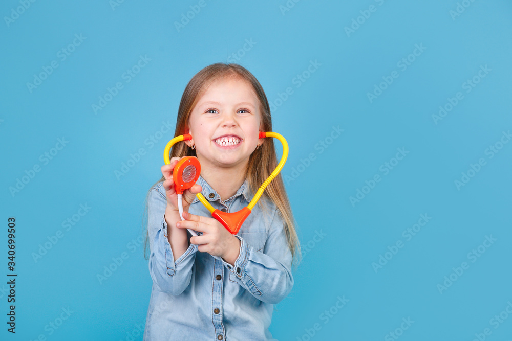 Smiling little girl holding stethoscope and looking at camera on blue background