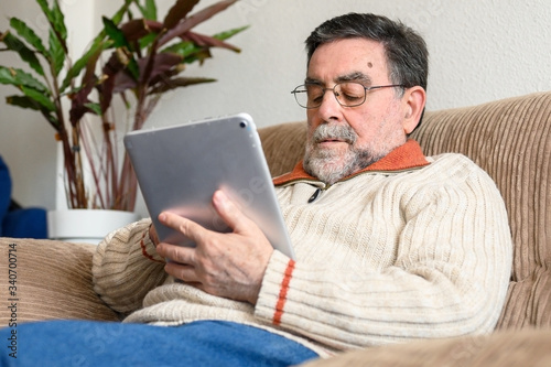 Portrait of senior man sitting on sofa and using digital tablet in living room .