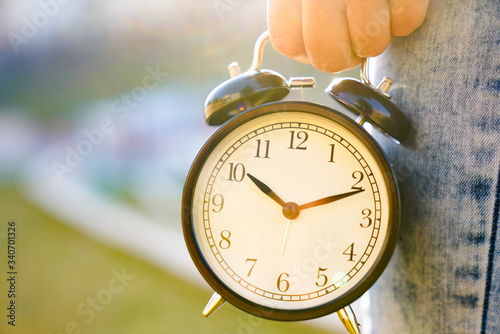 black alarm clock in a woman's hand on the background of nature. timeless and time concept image with beautiful woman taking a big vintage old black alarm and show to you the minutes going away. live  photo