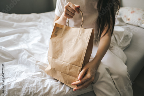 Woman holds craft eco shopping bag in hands, sitting at home on sofa. Delivery food