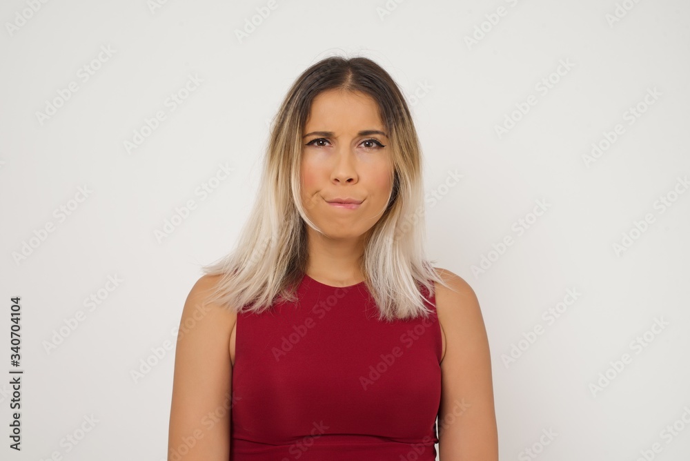 Obraz premium Pensive attractive blonde female being deep in thoughts, raises eyebrows, curves lips, wears fashionable clothes, stands against gray wall with copy space for your text.