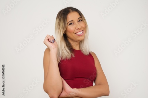 Image of cheerful pretty young caucasian lady standing against gray wall with hand near face. Looking with glad expression at the camera after listening to good news. Confident girl.