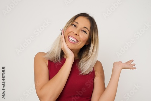 Positive glad female says: wow how exciting it is, has amazed expression, indicates something. Joyful pretty young woman demonstrates something. One hand on her head and pointing with other hand.