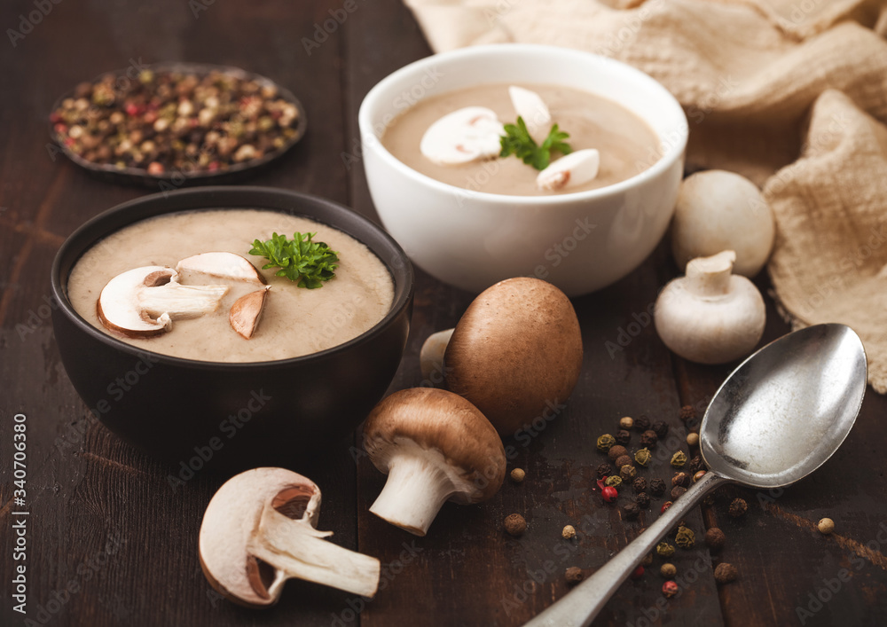 Ceramic bowl plates of creamy chestnut champignon mushroom soup with spoon, pepper and kitchen cloth on dark wooden background. Ceramic bowl plates of creamy chestnut champignon mushroom soup with spoon, pepper and kitchen cloth on dark wooden background.