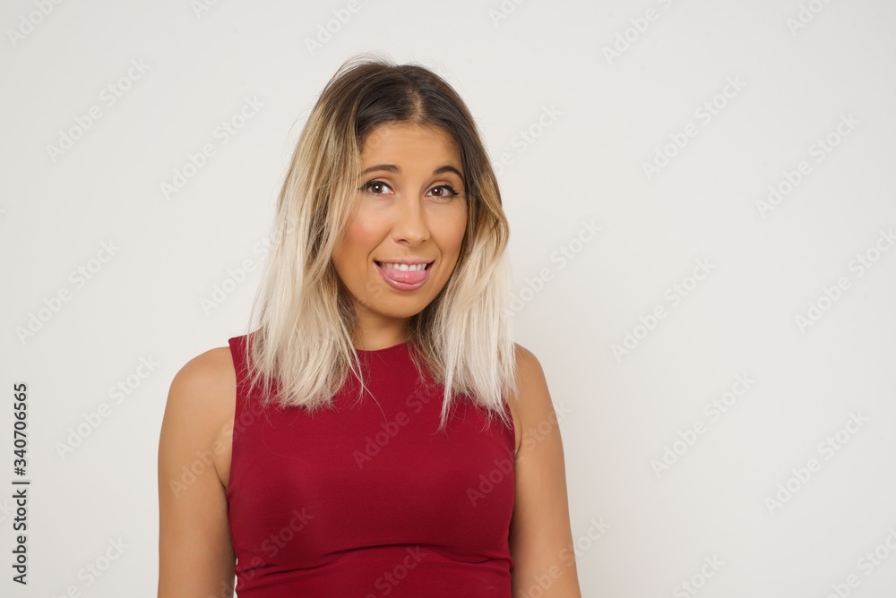 Beautiful Young caucasian woman with happy and funny face smiling and showing tongue. Wearing casual clothes and standing against gray studio background. Beautiful Young caucasian woman with happy and funny face smiling and showing tongue. Wearing casual clothes and standing against gray studio background.