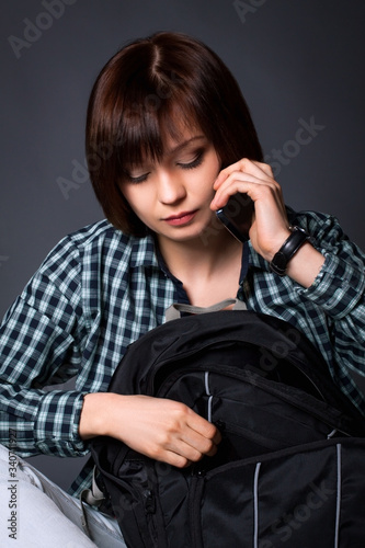 A college student is talking on a cell phone. Brunette girl in casual wear with a backpack.