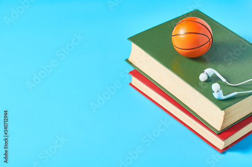 White headphone and old books, toy basketball ball on blue background. Audiobook concept. Online education. E-learning. Modern technology © OlekStock