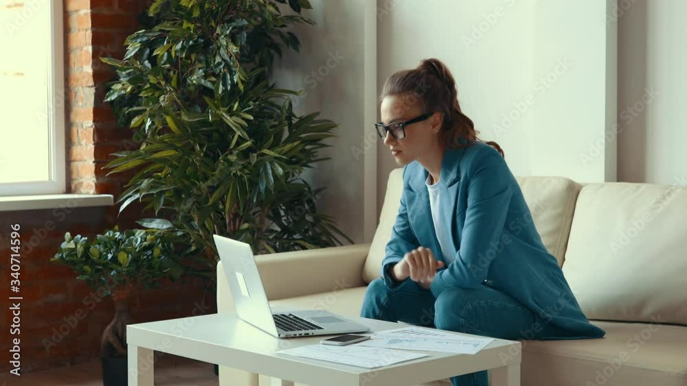 Young female in blue suit smiling and clenching fists then making phone call to share success after finishing remote project on laptop at home Young female in blue suit smiling and clenching fists then making phone call to share success after finishing remote project on laptop at home