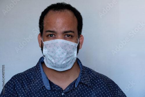 Covid-19 Corona virus pandemic facemask personal protective equipment mask mixed race male with beard wearing blue shirt skeptic expression face