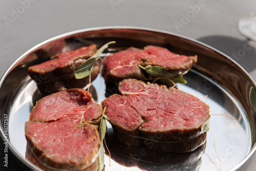 Four prepared tenderloin steaks ready for barbecue on silver plate on grey surfaced table