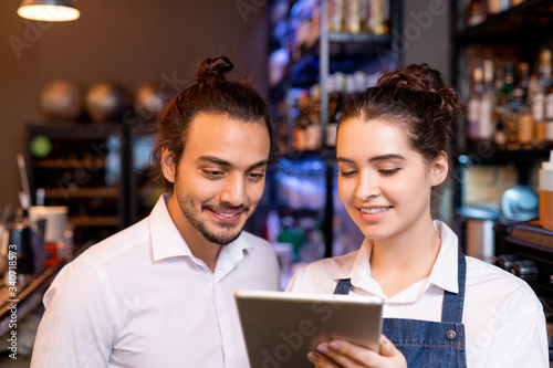 Happy young waitress with tablet showing her colleague new points in online menu