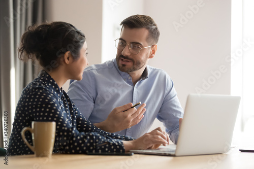 Different ethnicity millennial co-workers indian woman and caucasian man sit at desk discuss new project or task, share information brainstorm creative innovative ideas, teamwork and thinking concept