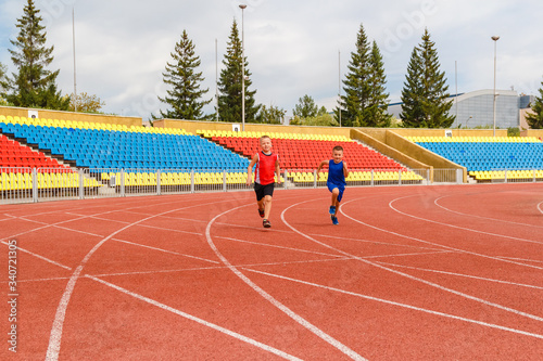 funny children run a race around the sports stadium. children at the event. empty sports stands. © Alyona
