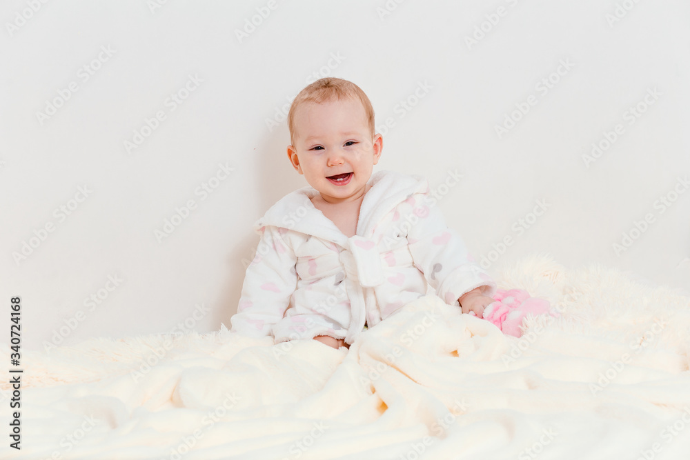 baby girl in a Terry robe and a diaper sitting on the bed after bathing. eight-month-old Caucasian baby girl. first teeth baby girl in a Terry robe and a diaper sitting on the bed after bathing. eight-month-old Caucasian baby girl. first teeth