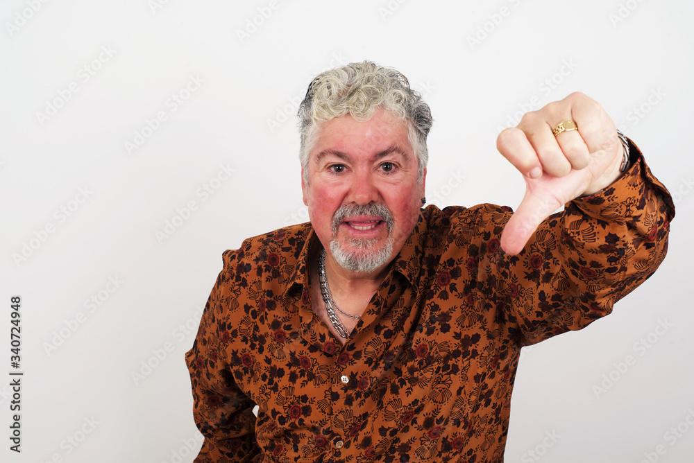 Discontent European man shows disapproval sign, keeps thumb down, expresses dislike, frowns face in discontent, dressed in white shirt, isolated over gray background. Body language concept. Discontent European man shows disapproval sign, keeps thumb down, expresses dislike, frowns face in discontent, dressed in white shirt, isolated over gray background. Body language concept.