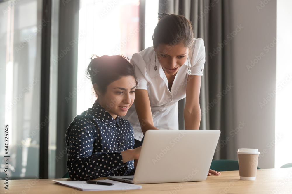 Multi-ethnic associates work together use laptop corporate application look at screen discuss task share ideas, mentor woman skilled ceo help to indian apprentice, give advice, explain program concept