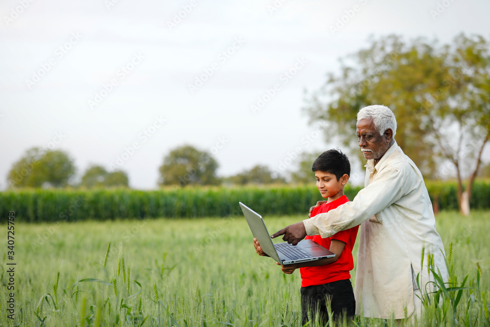 indian farmer with his grand son at wheat field, using laptop indian farmer with his grand son at wheat field, using laptop