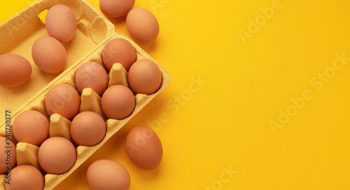 Print op canvas Brown chicken eggs in cardboard box on yellow background, top view