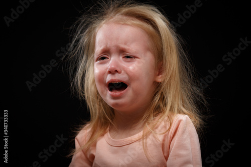 Emotional toddler child girl crying or screaming with mouth open, dark background
