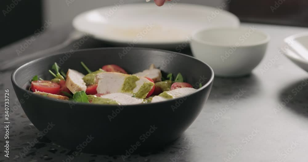 Slow motion almond flakes falling on salad with chicken, arugula and tomatoes in black bowl Slow motion almond flakes falling on salad with chicken, arugula and tomatoes in black bowl