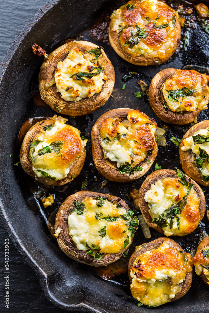 Baked champignons mushrooms, filled with cheese, parsley and roasted garlic in black bowl.