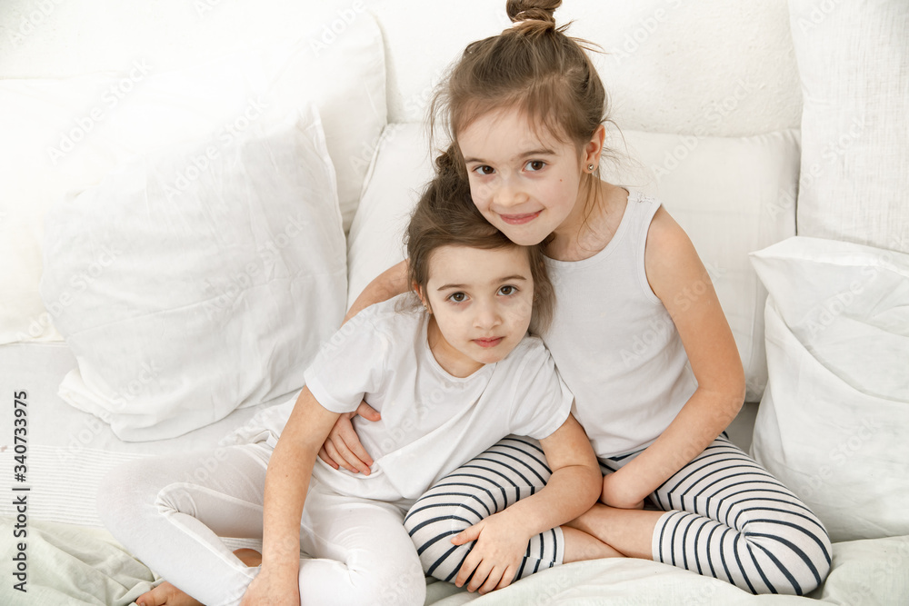 Two cute little sister girls cuddle on the bed in the bedroom. Two cute little sister girls cuddle on the bed in the bedroom.