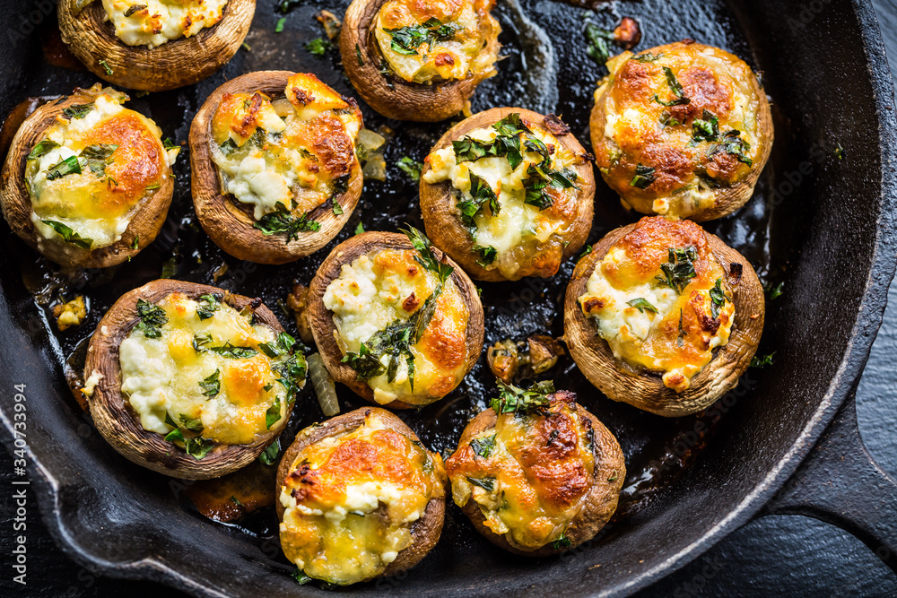 Baked champignons mushrooms, filled with cheese, parsley and roasted garlic in black bowl. Baked champignons mushrooms, filled with cheese, parsley and roasted garlic in black bowl.
