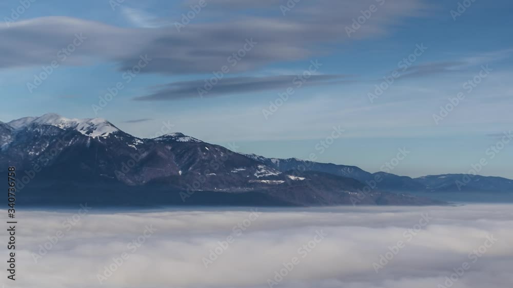 Zoom out time lapse over sea clouds. In background Alps mountain range in Slovenia. Winter season mountains covered with snow Zoom out time lapse over sea clouds. In background Alps mountain range in Slovenia. Winter season mountains covered with snow