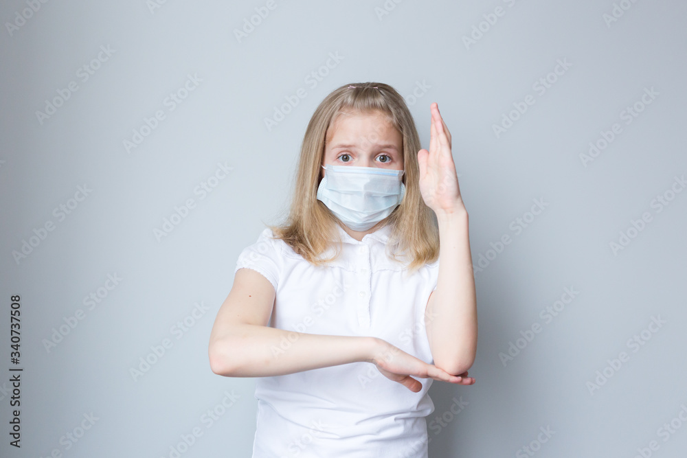 The schoolgirl wants to answer a question, pulls a hand. There is a mask on her face. Online education. Grey background. The schoolgirl wants to answer a question, pulls a hand. There is a mask on her face. Online education. Grey background.