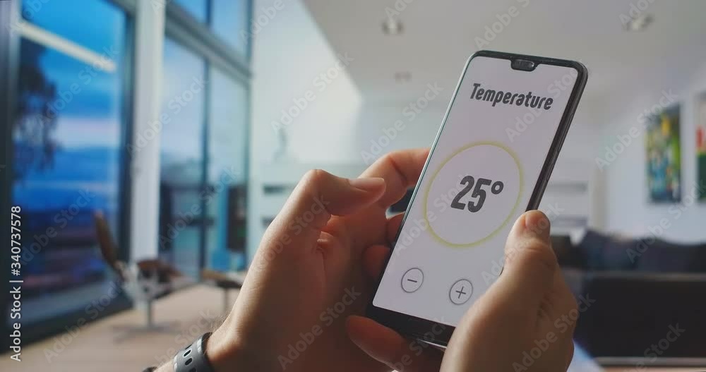 Smart home, application on the phone. A man manages various parameters of his home from a smartphone. Smart home. Man holding phone with app smart home on screen in room house