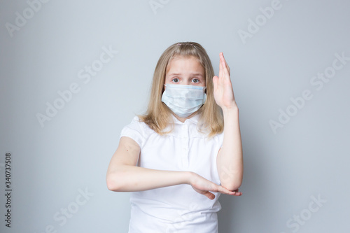 The schoolgirl wants to answer a question, pulls a hand. There is a mask on her face. Online education. Grey background.
