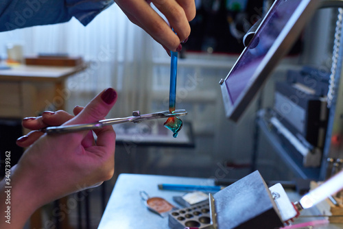 Hands of young female lampworking master cutting lower end of blue glass tube photo