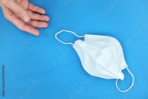 Billede på lærred Hand laying down a white face mask on blue table background
