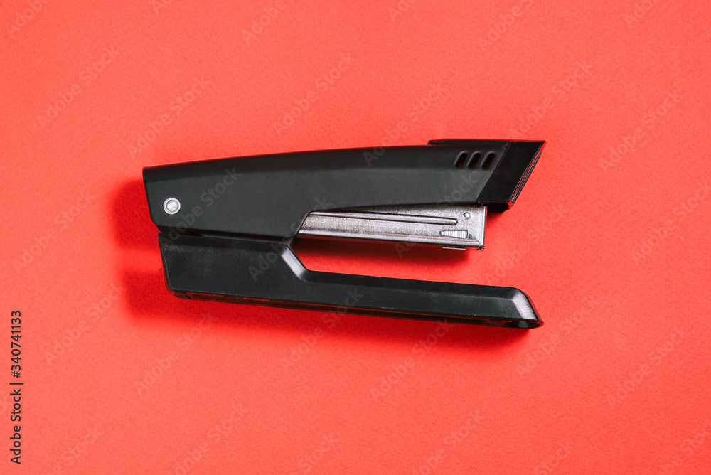 Large black office stapler on a red background. Stationery for stapling paper. Accessories for work. Large black office stapler on a red background. Stationery for stapling paper. Accessories for work.