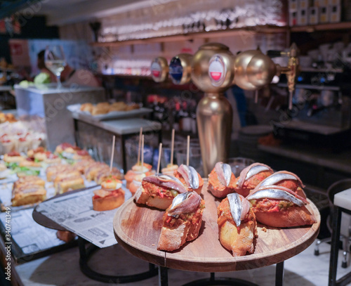 Traditional spanish snacks, appetizers or tapas called pintxos in a bar or cafe in San Sebastian, Basque country, Spain. Anchovy sandwich on a bar counter in a typical restaurant or tapas bar.