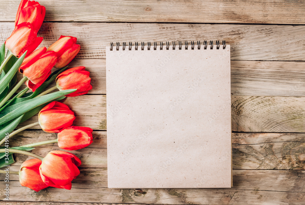 Real spring red tulips and empty notebook on a rustic wooden background. Spring flowers for Mother's Day. Top view Real spring red tulips and empty notebook on a rustic wooden background. Spring flowers for Mother's Day. Top view