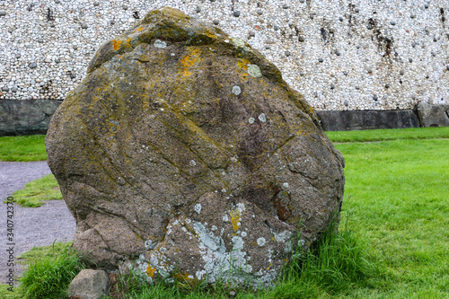 A large weathered standing stone in front of Newgrange megalithic passage tomb in the Boyne Valley, Meath, Ireland. The dazzling white quartz stone wall of the earth mound is in the background. photo