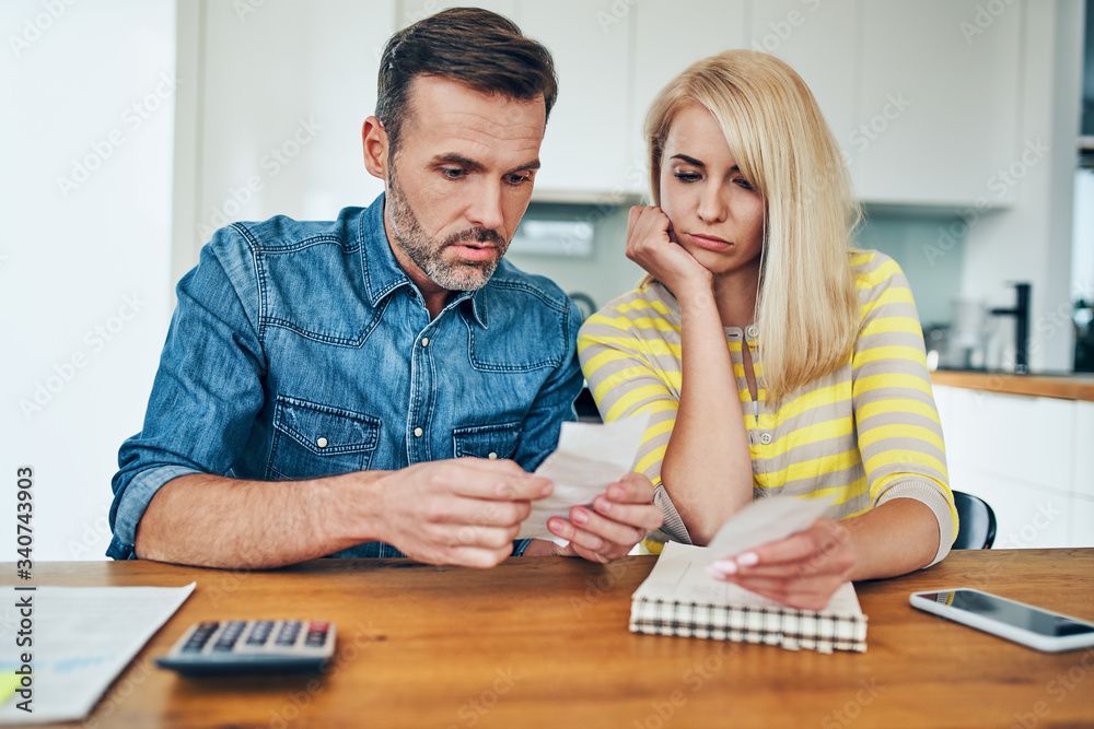 Sad couple looking at store receipt while managing home finances worried about money Sad couple looking at store receipt while managing home finances worried about money