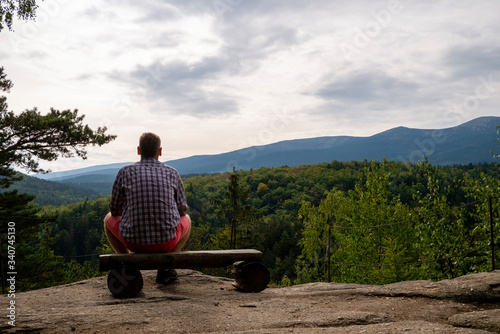 man in red trousers sitting on a bench overlooking the green mountains