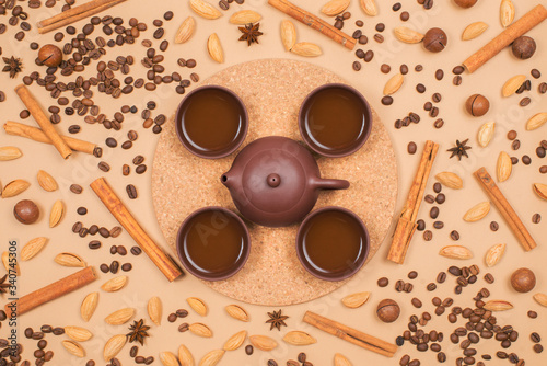 Flat lay tea set - clay tea pot with tea cups. Coffee beans, cinnamon, almond and macadamia on background. Top view
