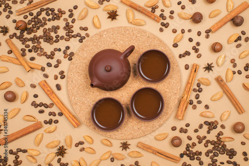 Top view tea set - clay tea pot with tea cups. Coffee beans, cinnamon, almond and macadamia on background. Top view