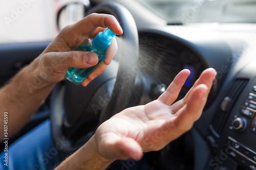 Close up of hands holding and using alcohol antibacterial spray bottle inside of car.