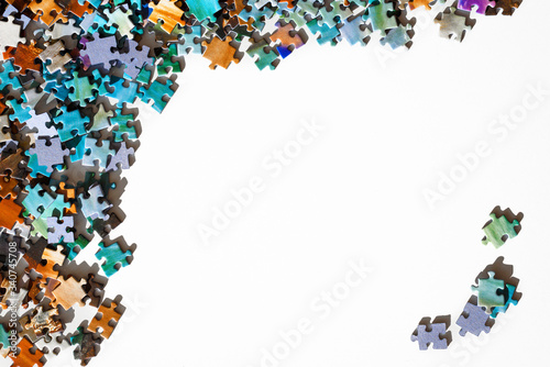 Top view of scattered multicolored jigsaw puzzle pieces. Lying on white table arranged as frame for copy space. Concept of putting together disconnect elements. photo
