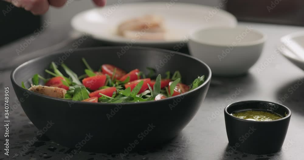 Slow motion man hands put cherry tomatoes over fresh arugula in black bowl on concrete countertop Slow motion man hands put cherry tomatoes over fresh arugula in black bowl on concrete countertop