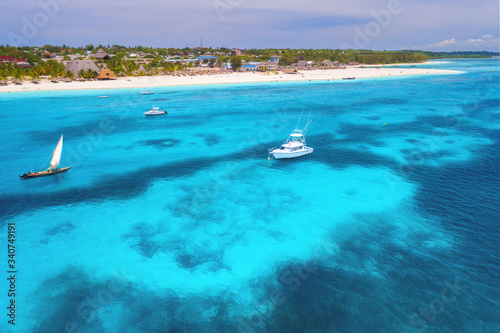 Aerial view of boats and yachts on tropical sea coast with sandy beach at bright sunny day in summer. Indian Ocean in Africa. Landscape with boat, palm trees, clear blue water, sky. View from above