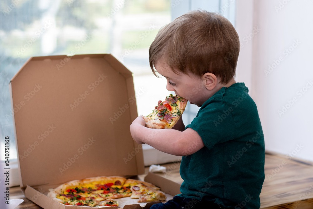 little boy eating a slice of pizza at the window.