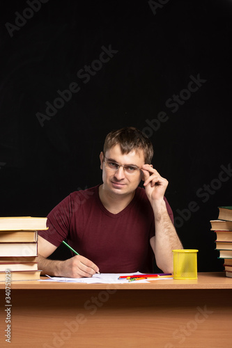 young student sits at a table with books. one hand holds glasses. vertical photo. Black background. isolate.