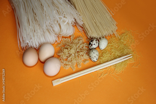 rice noodles all kinds of macaroni and macaroni with chicken, quail eggs and chopsticks on an orange background